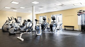 Une salle de sport équipée de divers appareils d’exercice, d’un banc et d’une fenêtre.
