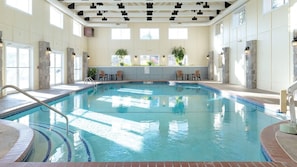 Une piscine intérieure avec un bord carrelé, une échelle en métal et des chaises disposées autour de la piscine.