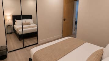 A modern bedroom with a large bed, a mirror, a bedside table, and a door leading to another room.