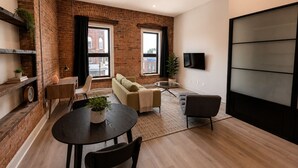 Una sala de estar moderna con pared de ladrillo, un sofá, un televisor y una zona de comedor con mesa y sillas.