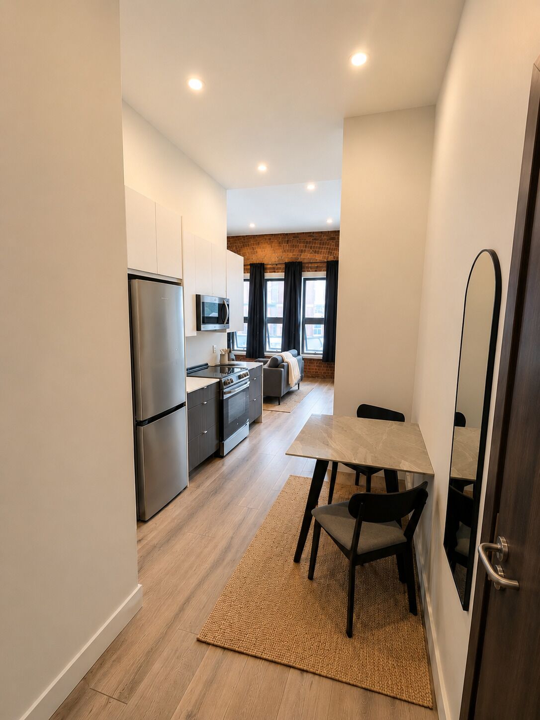 A compact kitchen with modern appliances, a dining area with a table and chairs, and a large mirror on the wall.