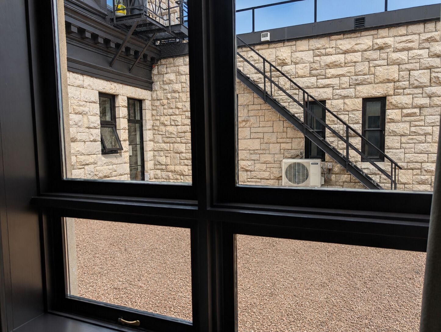 A window view of a building with stone walls, a staircase, and an air conditioning unit.