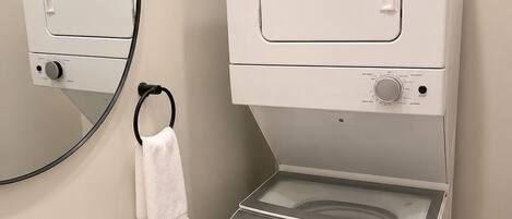 A bathroom with a sink, mirror, towel rack, and a white washing machine.