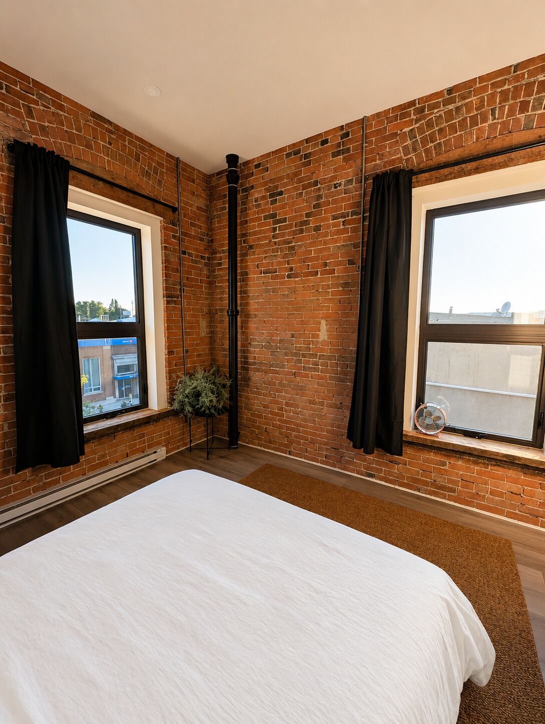 A bedroom with a large bed, brick walls, and two windows with black curtains.