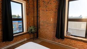 A bedroom with a large bed, brick walls, and two windows with black curtains.