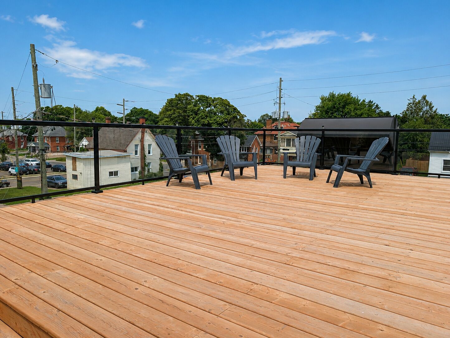 Um deck de madeira com cadeiras Adirondack, uma área coberta e vista para casas e linhas de energia.