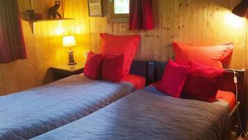 Une chambre avec deux lits, des murs en bois, une fenêtre avec des rideaux, une lampe et une petite étagère avec quelques objets.