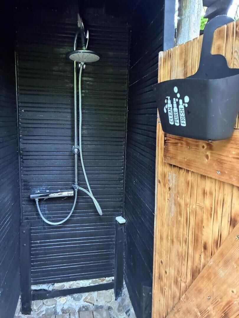 A wooden structure with a black exterior, a showerhead, and a black container with white text.