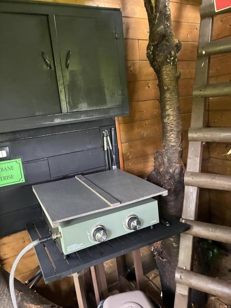 Una habitació amb un armari verd, una taula amb un aparell i una escala adossada a una paret de fusta.
