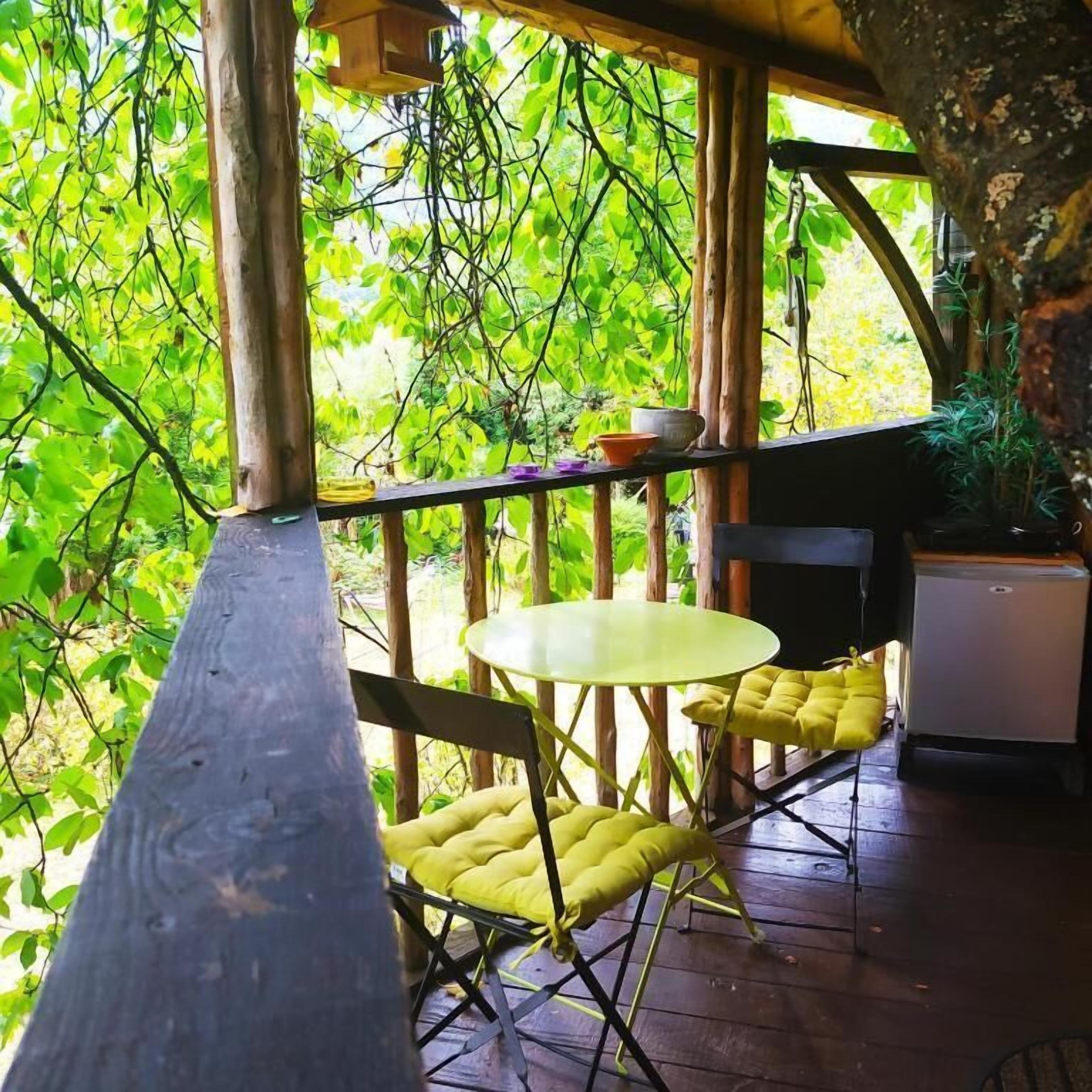 An outdoor wooden deck with a table and chairs, surrounded by lush greenery.