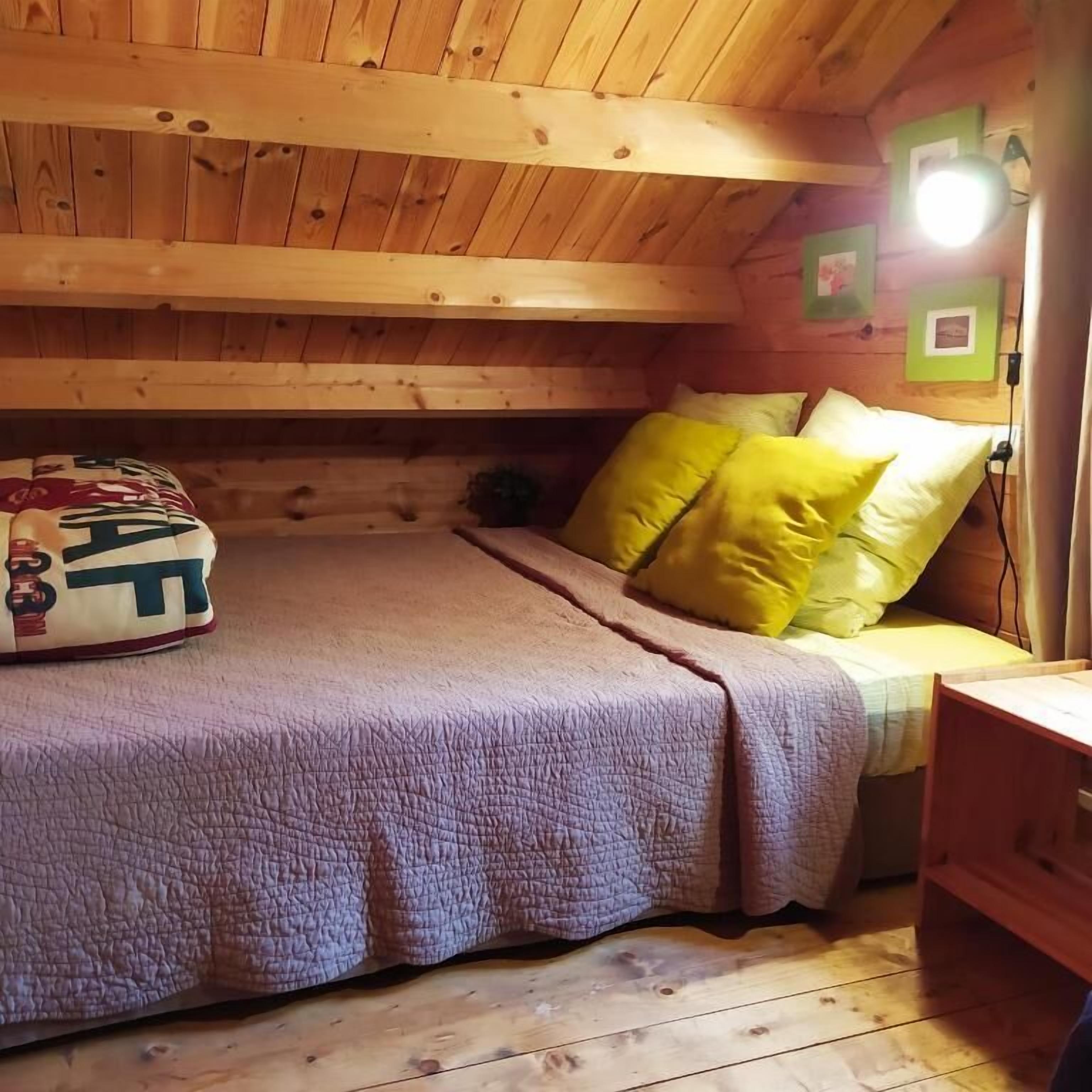 L’intérieur d’une cabane en bois, avec un lit, des oreillers et une table de chevet.