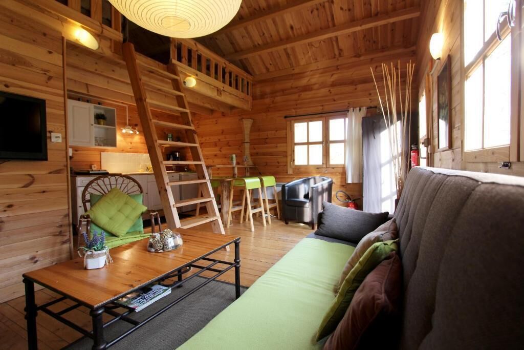 A wooden cabin interior with a sofa, a dining table, a ladder, and a television.