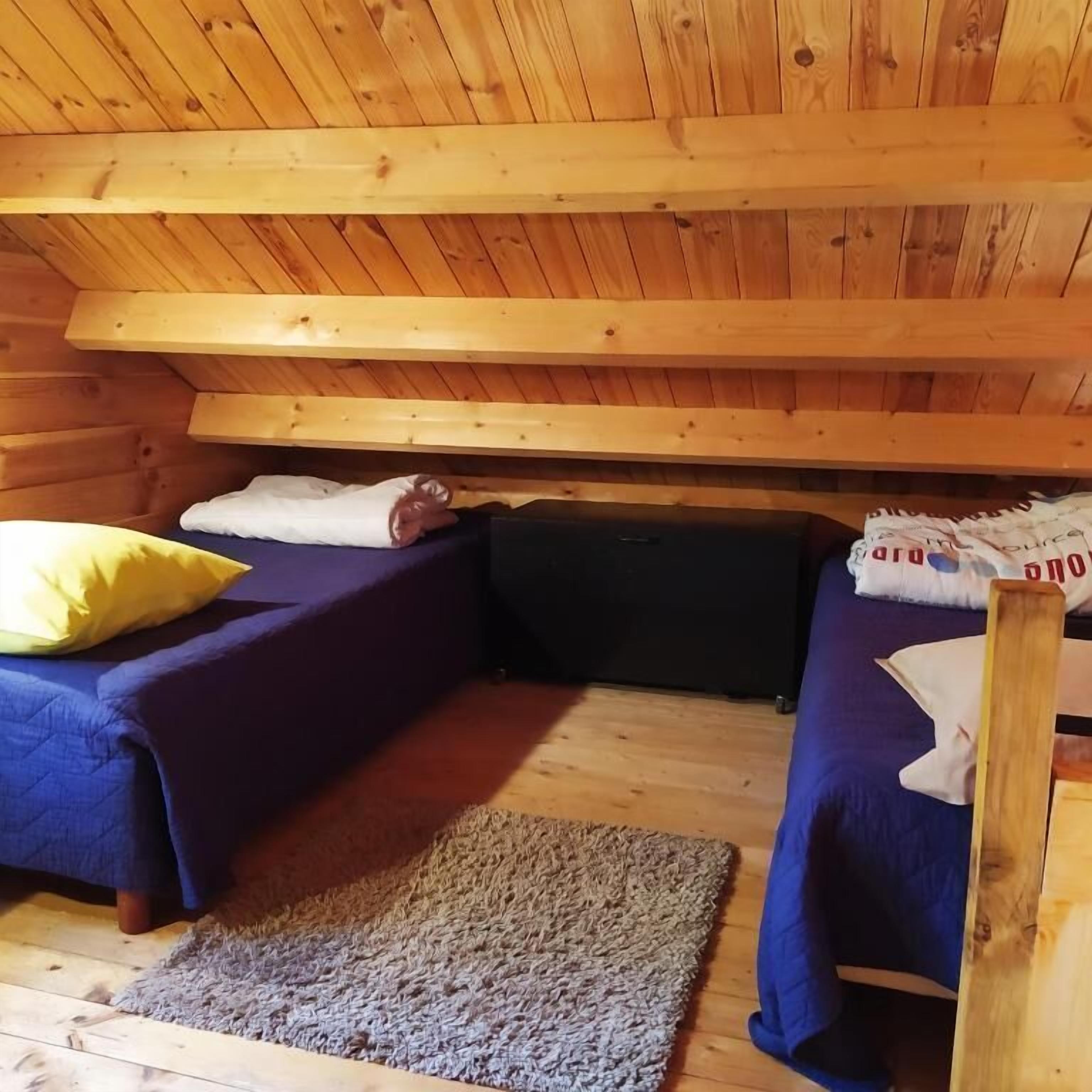 A cabin with two beds, a wooden ceiling, and a rug on the floor.