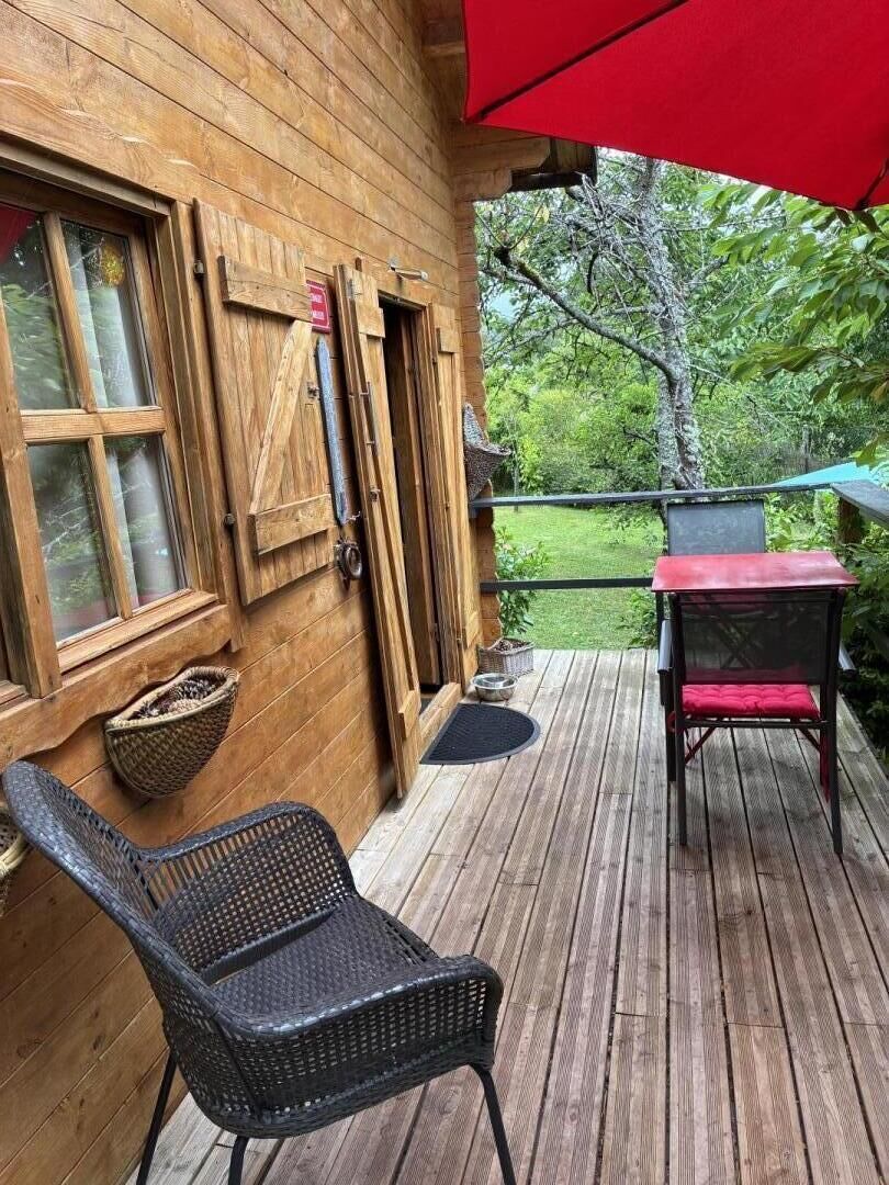 Une terrasse en bois avec une chaise en osier et une table agrémentée d’un coussin rouge.