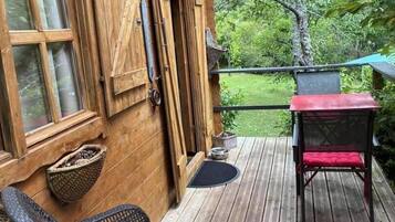 Una terraza de madera con una silla de mimbre y una mesa con cojín rojo.