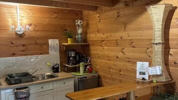 A wooden interior with a kitchen area, including a sink, cabinets, and a dining table with stools.