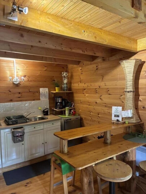 Puisesti sisustettu tila, jossa on keittiöalue, johon kuuluu pesuallas, kaappeja sekä ruokapöytä ja -jakkarat.