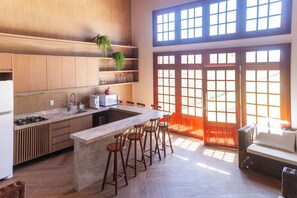 A modern kitchen with a central island, bar stools, wooden cabinetry, and a large window with a view. - Seaside Retreat w4 Bedrooms and Pool (Caponga)