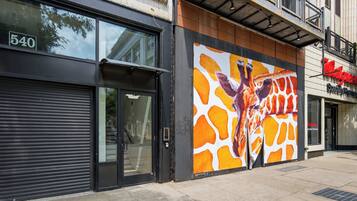 Um edifício com um grande mural de girafa na lateral, uma entrada com persianas fechadas e uma farmácia Walgreens na rua.