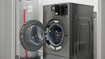 Máquina de lavar roupa com carga frontal, porta fechada, painel de comandos e mangueira de entrada de água.