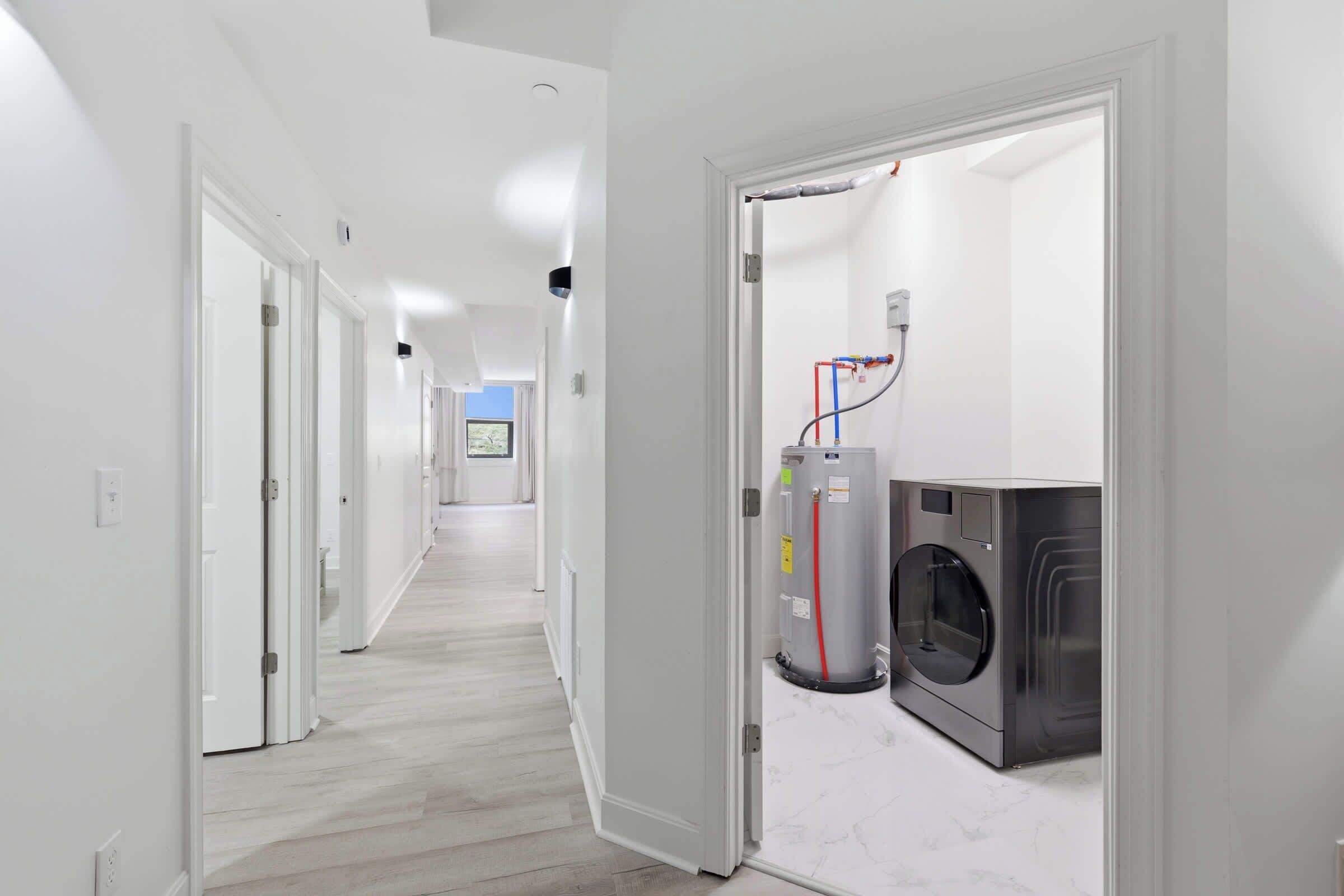 Um corredor de hotel com uma lavanderia, incluindo máquina de lavar e secadora, um aquecedor de água visível e uma porta que dá para um quarto com vista.