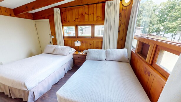 A wooden cabin room with two beds, a nightstand, and a window with curtains. - Cozy 1-bedroom hotel room in awesome Hamilton - #327 Susquehanna (Hamilton)