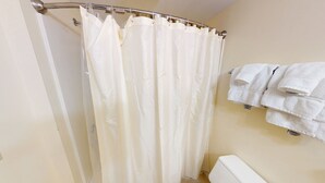 A bathroom with a shower curtain, a toilet, and a towel rack with towels. - Cozy 1-bedroom hotel room in awesome Hamilton - #327 Susquehanna (Hamilton)