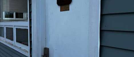 Une porte blanche avec une boîte aux lettres et un panneau indiquant qu’il est interdit de fumer.