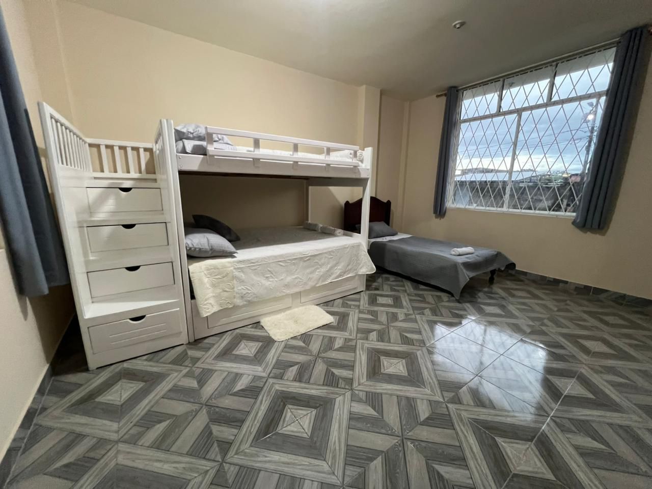A room with bunk beds, a window, and patterned flooring.