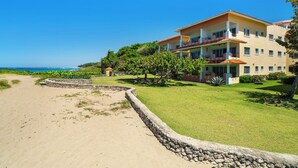 Ein Strandhotel mit Steinmauer, Rasenfläche und freiem Blick auf den Ozean.