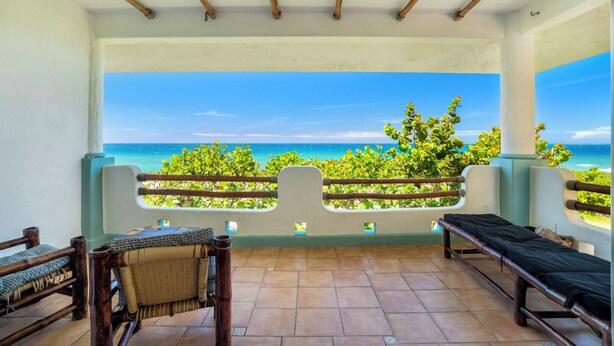 Ein Balkon mit Blick auf das Meer, ein Korbstuhl, eine Bank und ein Fliesenboden.