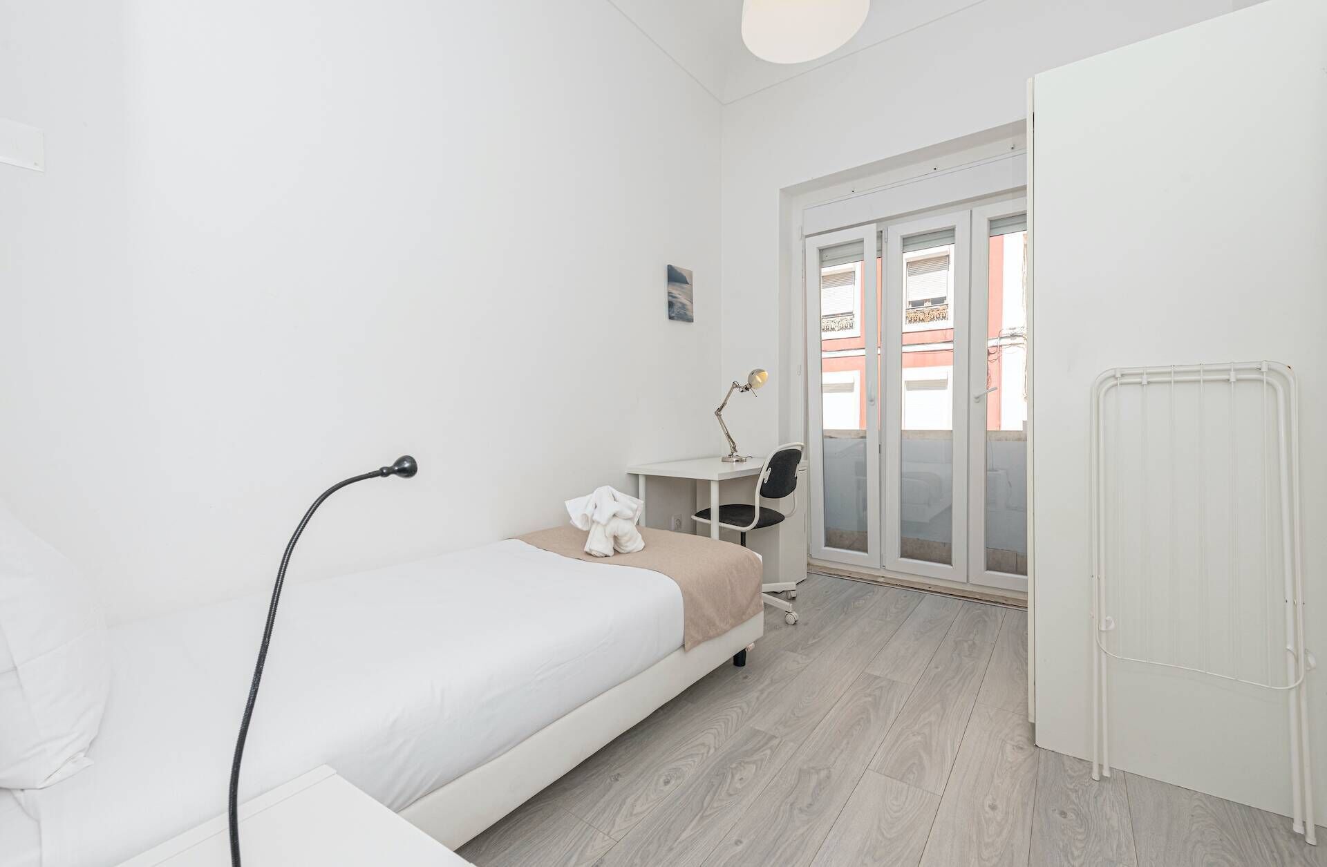 Camera d'albergo dallo stile minimalista con un letto, una scrivania, una sedia, un termosifone e vista attraverso una porta in vetro.