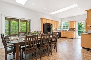 Une cuisine spacieuse avec des meubles en bois, un coin repas doté d’une grande table et de chaises, et une vue sur la verdure environnante.