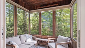 A wooden-paneled room with a large window, a sofa, a chair, and a small table. - WoodPark Cottage 7bedroom Gamesroom (Lambton Shores)