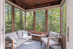 A wooden-paneled room with a large window, a sofa, a chair, and a small table. - WoodPark Cottage 7bedroom Gamesroom (Lambton Shores)