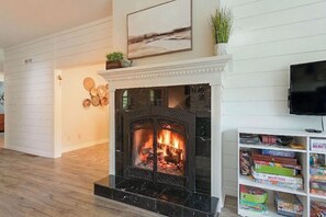 A living room with a fireplace, a television mounted on the wall, and a bookshelf with board games. - WoodPark Cottage 7bedroom Gamesroom (Lambton Shores)