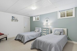 A bedroom with two beds, a dresser, a bench, and a door. - WoodPark Cottage 7bedroom Gamesroom (Lambton Shores)