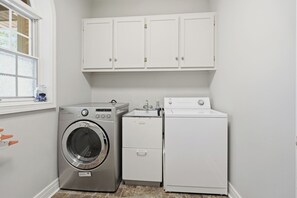 A laundry room with a front-loading washing machine, a dryer, and a cabinet above the machines. - WoodPark Cottage 7bedroom Gamesroom (Lambton Shores)