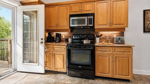 A kitchen with wooden cabinets, a microwave, a stove, and a toaster. - WoodPark Cottage 7bedroom Gamesroom (Lambton Shores)