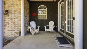 A porch with two Adirondack chairs, a red maple leaf decoration, and a window with a grid pattern. - WoodPark Cottage 7bedroom Gamesroom (Lambton Shores)