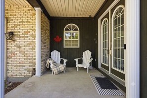A porch with two Adirondack chairs, a red maple leaf decoration, and a window with a grid pattern. - WoodPark Cottage 7bedroom Gamesroom (Lambton Shores)