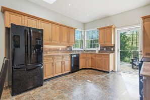 A spacious kitchen with wooden cabinets, a black refrigerator, and a dishwasher. - WoodPark Cottage 7bedroom Gamesroom (Lambton Shores)