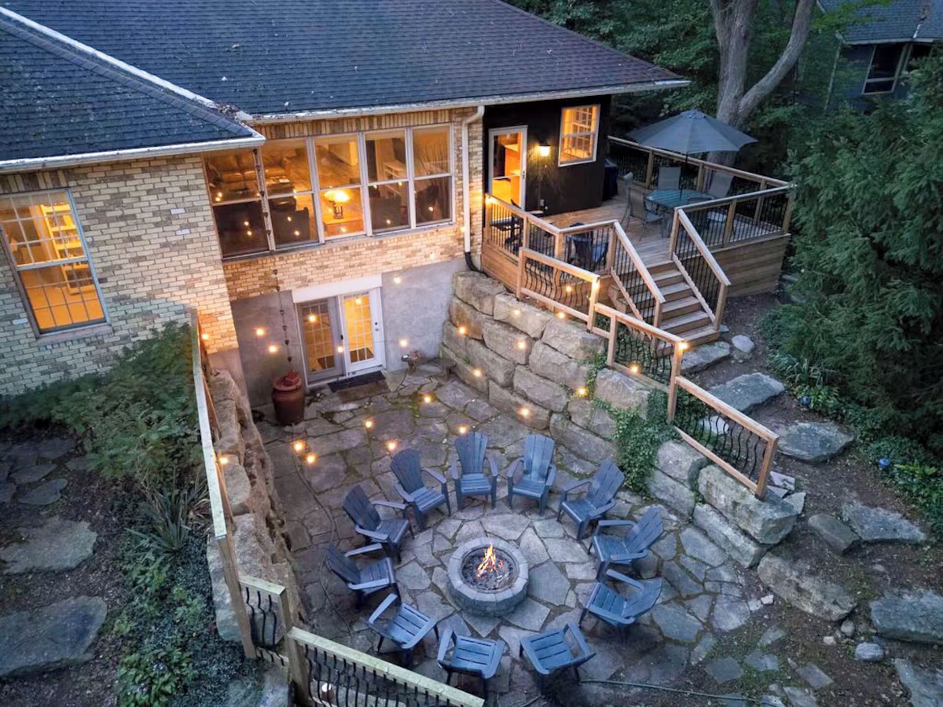 Een huis met een stenen terras, buitenmeubels en een vuurkuil.
