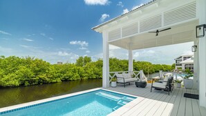 Et poolområde med overdækket terrasse, liggestole og udsigt til et vandareal.