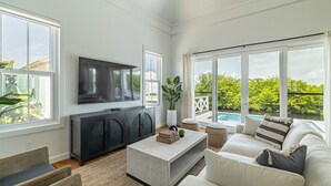En moderne stue med et fladskærms-TV, en sofa, et sofabord og udsigt til en swimmingpool.