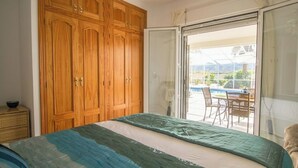 Ein Schlafzimmer mit einem Bett, einem Holzschrank und einer Schiebetür zu einem Außenbereich mit Tisch und Stühlen.