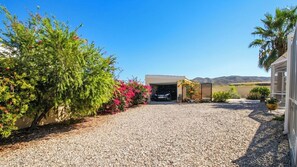A driveway leading to a garage with a vehicle parked inside, surrounded by gravel and various plants. - Villa Kara Arboleas by Ruralidays (Almería)