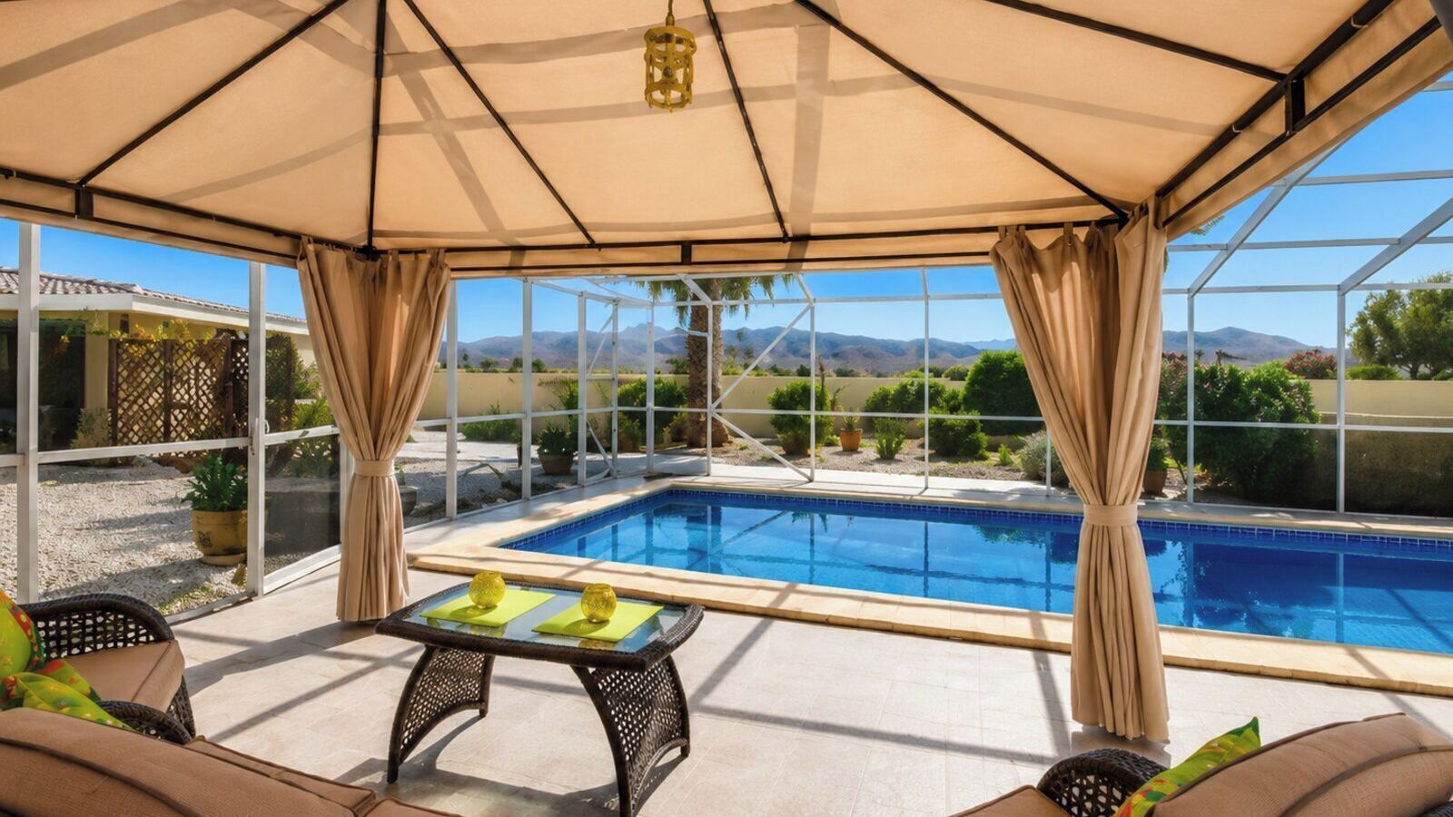 A covered outdoor pool area with a table and chairs, a view of the pool, and a patio with a pergola.