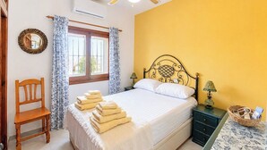 Een slaapkamer met een bed, een stoel, een nachtkastje, een lamp en een raam met gordijnen.