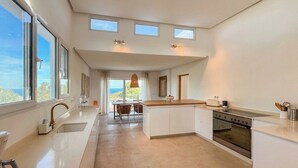 Een moderne keuken met een centraal eiland, een eethoek met uitzicht en een groot raam.
